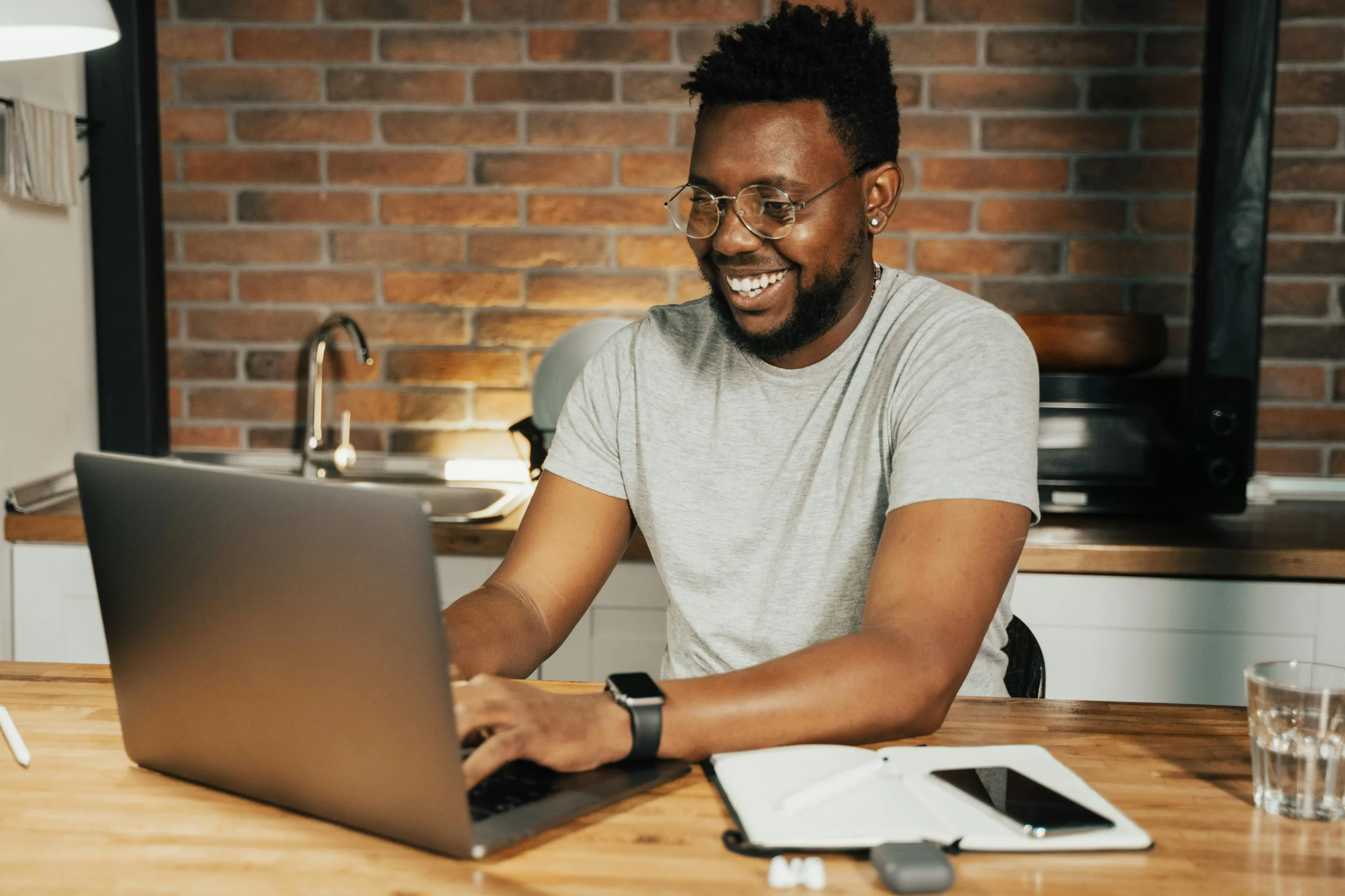 Man, smiling, looking at his laptop, following an online course in his kitchen.